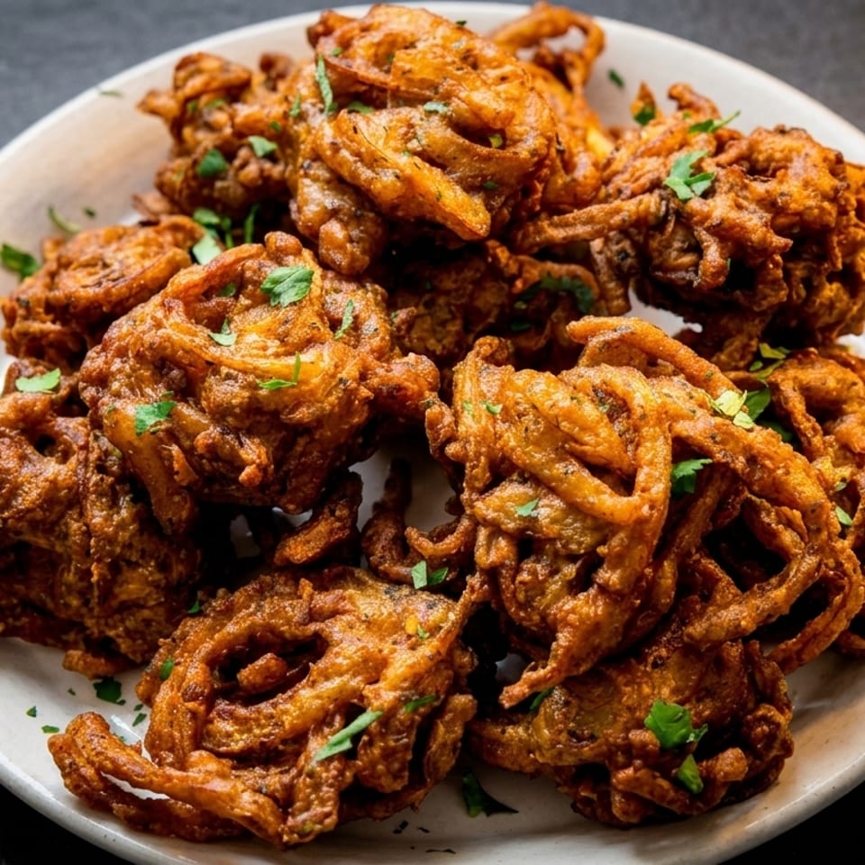 A white plate filled with golden-brown, crispy onion bhaji, garnished with fresh parsley.