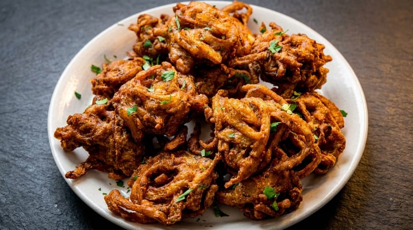 A white plate filled with golden-brown, crispy onion bhaji, garnished with fresh parsley.