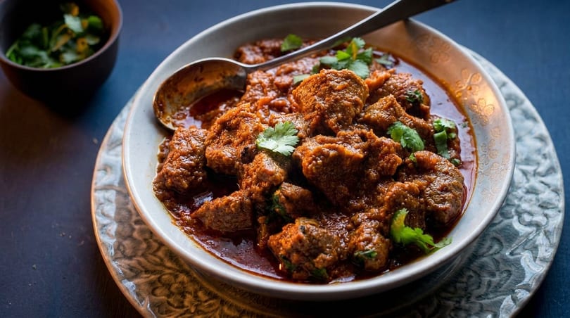 A bowl of rich, red curry with chunks of meat and fresh cilantro, with a spoon resting in it.